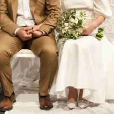 Para młoda siedzi obok siebie, trzymając się za ręce. Ona ma bukiet białych kwiatów. Czy można wziąć ślub na zwolnieniu lekarskim?