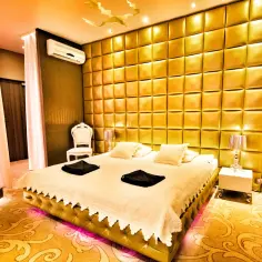 Luksusowy pokój hotelowy w Poznaniu z pikowaną złotą ścianą, wygodnym łóżkiem i eleganckim fotelem.