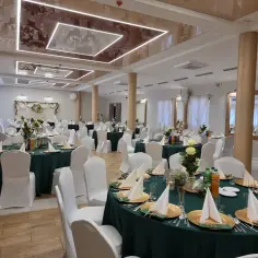 Elegancka sala bankietowa "Rancho pod Bocianem" gotowa na przyjęcie gości. Stoły nakryte zielonymi obrusami, ozdobione kwiatami i złotymi naczyniami.