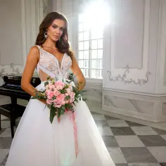 Przyszła panna młoda w sukni z koronkową górą i bukietem różowych kwiatów. Czy przymiarki sukien ślubnych są płatne?
