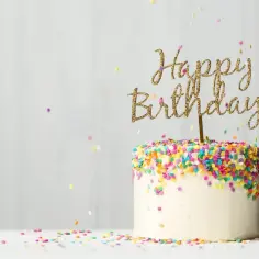 Biały tort urodzinowy z kolorową posypką i złotym napisem "Happy Birthday". Zastanawiasz się, ile kosztuje kilogram torta?