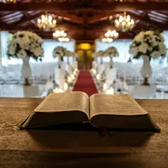 Otwarta Biblia na drewnianym stole. W tle udekorowana sala, gdzie za chwilę rozpocznie się msza. Ile trwa msza w kościele?