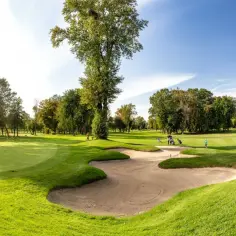 Piękny dzień na polu golfowym w Warszawie. Gracze cieszą się grą, a słońce oświetla zielone dołki i piaszczyste bunkry.