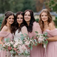 Cztery uśmiechnięte kobiety w różowych sukniach i panna młoda w białej sukni, trzymają bukiety. Czy można mieć dwóch świadków na ślubie? Tak, a nawet więcej!