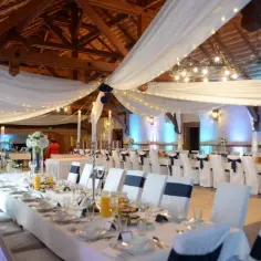 Uroczysta sala weselna w karczmie u Michelle. Długie stoły nakryte białymi obrusami, ozdobione świecami i kwiatami. Krzesła w eleganckich pokrowcach.