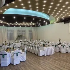 Elegancka sala bankietowa hotelu Jan Sander gotowa na przyjęcie gości. Stoły nakryte białymi obrusami, krzesła w pokrowcach z zielonymi kokardami.