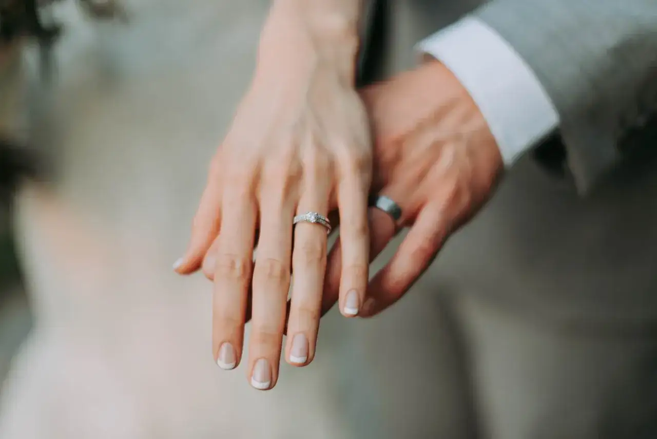 Dłonie nowożeńców z obrączkami. Delikatny manicure i błyszczący pierścionek na palcu panny młodej. Co oznacza miesiąc ślubu?