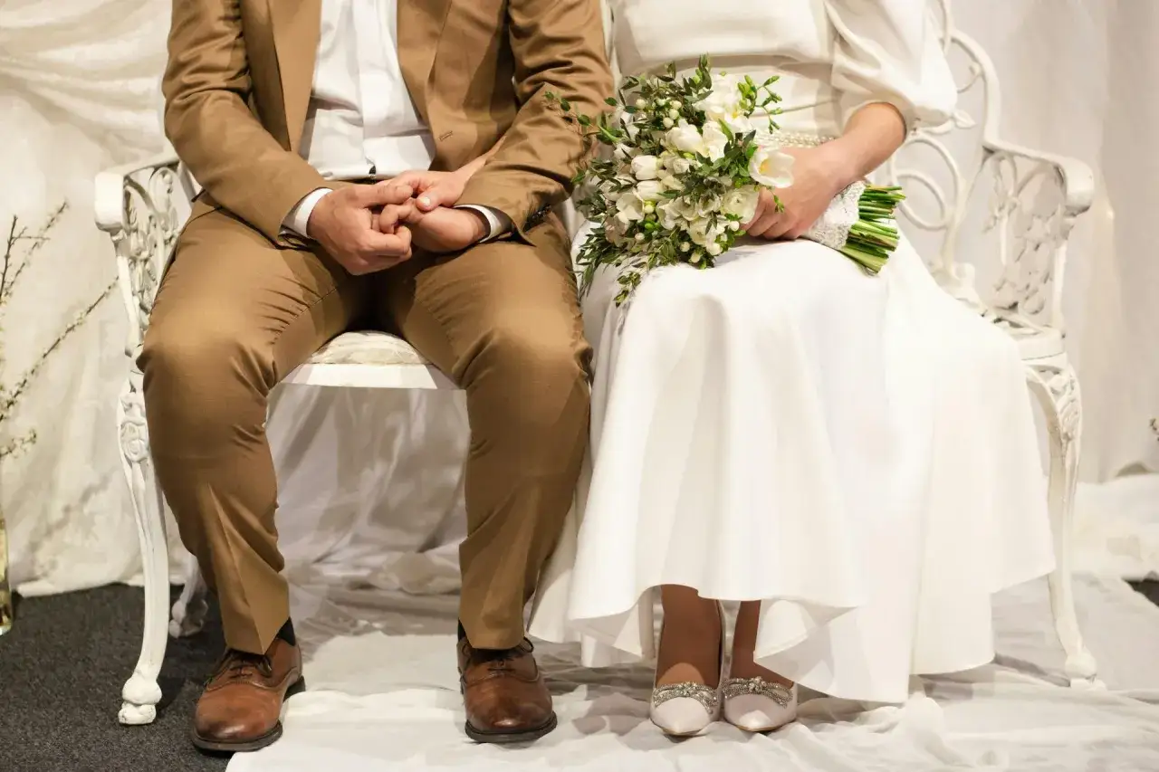 Para młoda siedzi obok siebie, trzymając się za ręce. Ona ma bukiet białych kwiatów. Czy można wziąć ślub na zwolnieniu lekarskim?