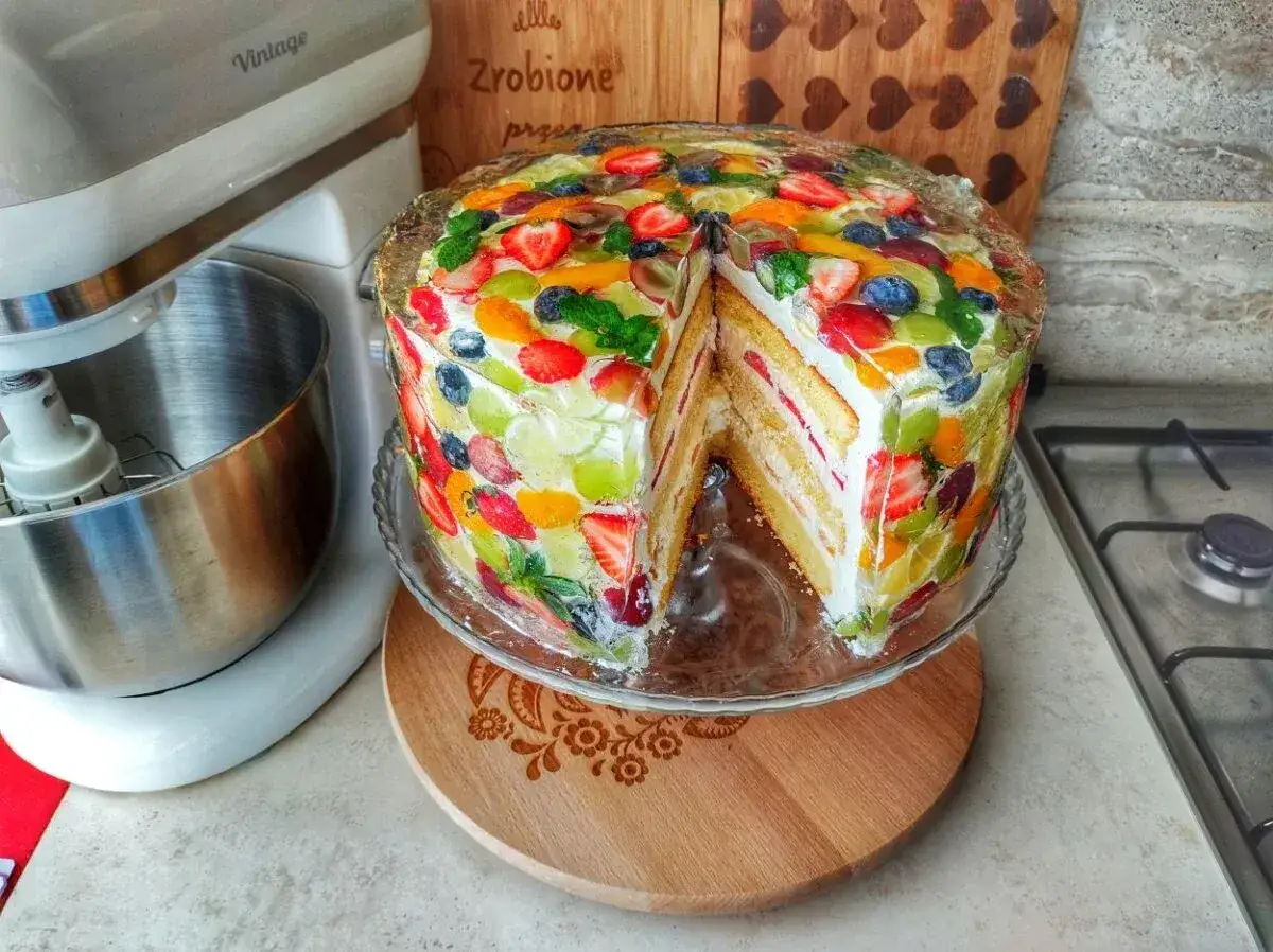 Kolorowy tort z owocami w galaretce, idealny na początek przygody, jak zacząć robić torty. Obok mikser planetarny.