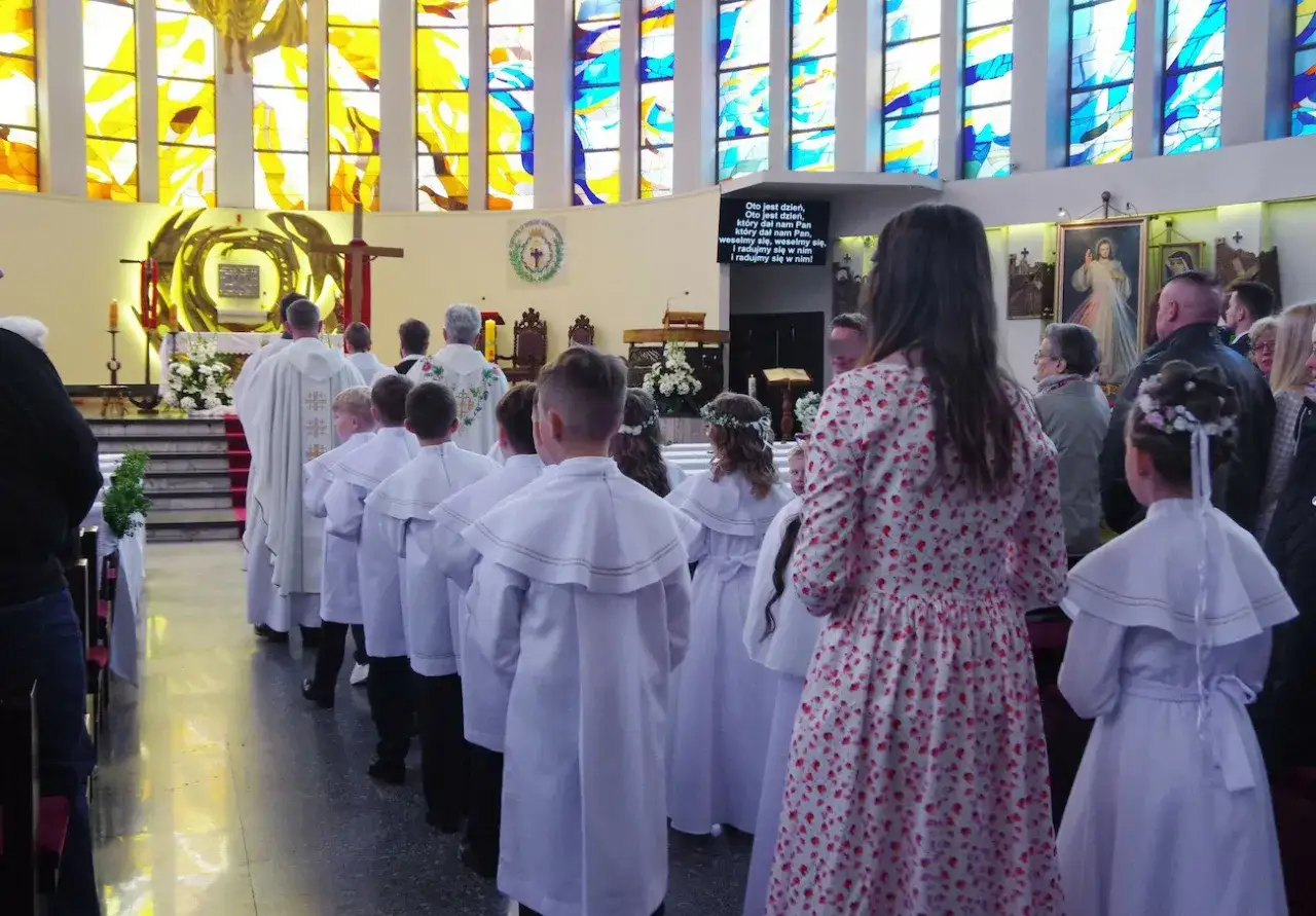 Dzieci w białych strojach idą do komunii w kościele.