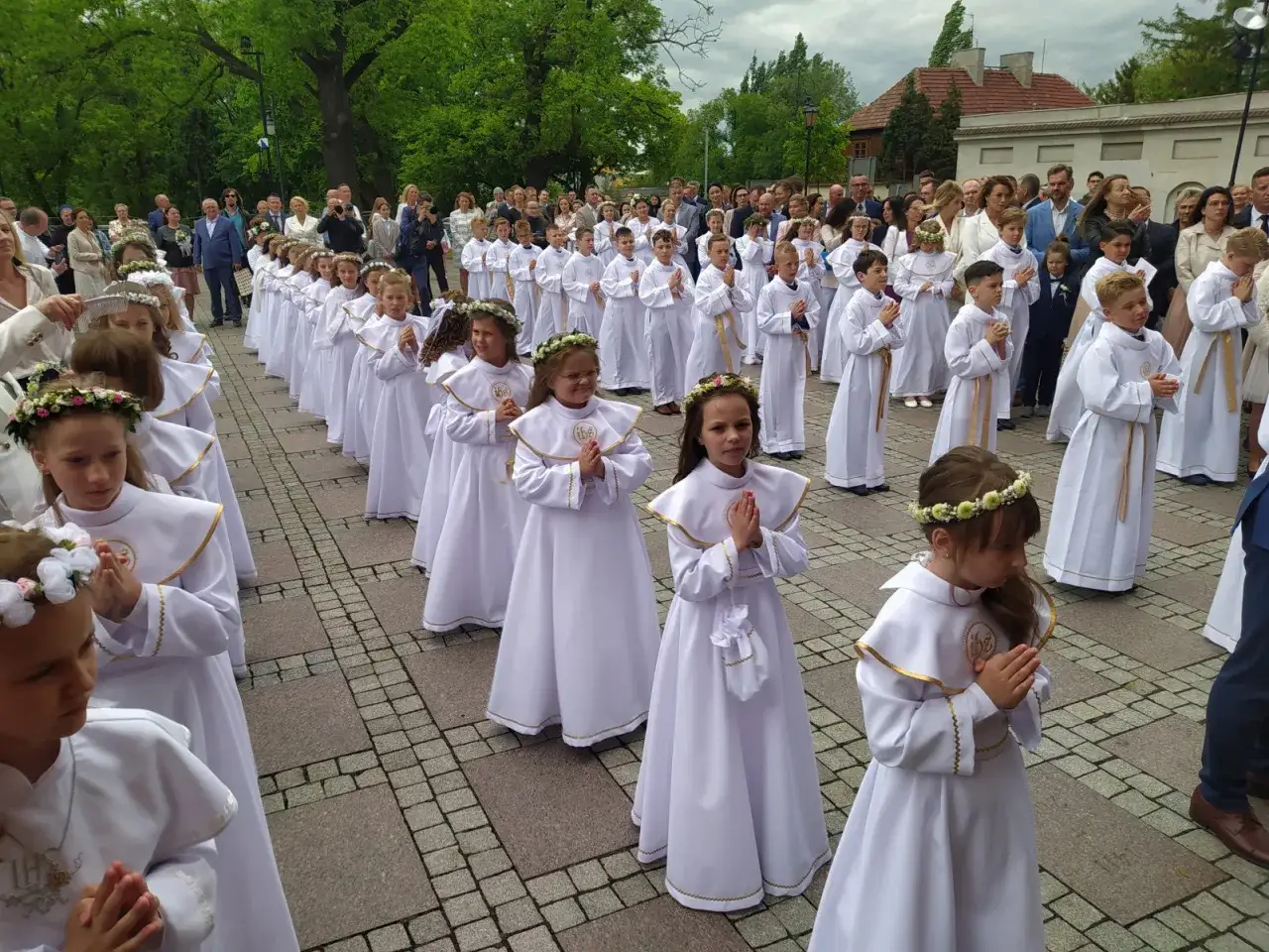 Dzieci w białych strojach, gotowe na komunię w której klasie. Wianki na głowach, modlitewne dłonie.