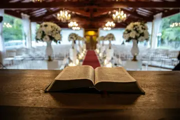 Otwarta Biblia na drewnianym stole. W tle udekorowana sala, gdzie za chwilę rozpocznie się msza. Ile trwa msza w kościele?