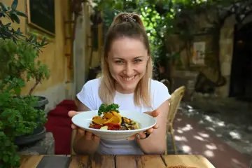 Uśmiechnięta kobieta prezentuje talerz z warzywami z grilla i pomarańczą. W tej restauracji wiesz, co zjesz – pyszne i zdrowe dania.