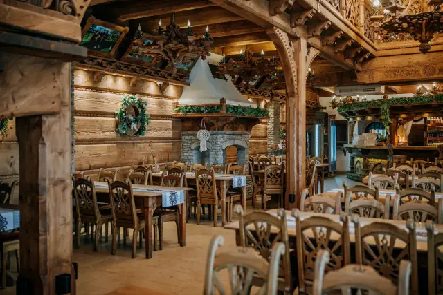 Drewniana, przytulna restauracja "Przystań w Kabanosie" z kamiennym kominkiem i tradycyjnymi zdobieniami.